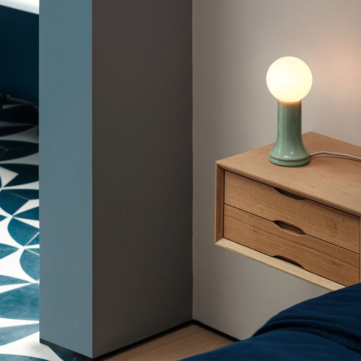 Mouth-blown glass table lamp in sea green, on a wall-hung shelf unit