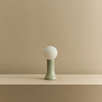 Mouth-blown glass table lamp in sea green, unlit, on a shelf