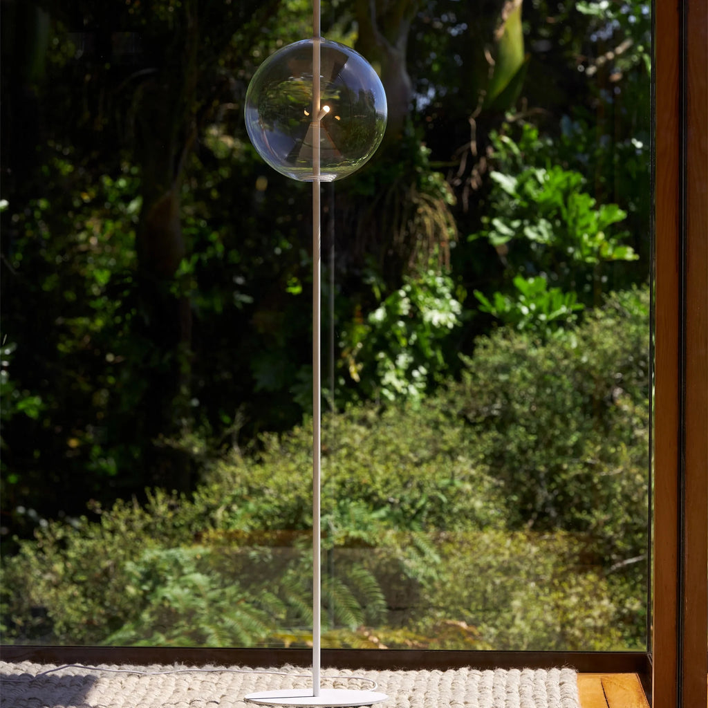 Single globe floor lamp in mouth-blown glass, in clear glass by a garden door