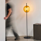 Single globe floor lamp in mouth-blown glass, in amber glass with a person passing