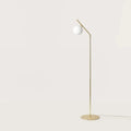 Slim articulated floor lamp with opal glass globe, matte brass, unlit, three-quarter view