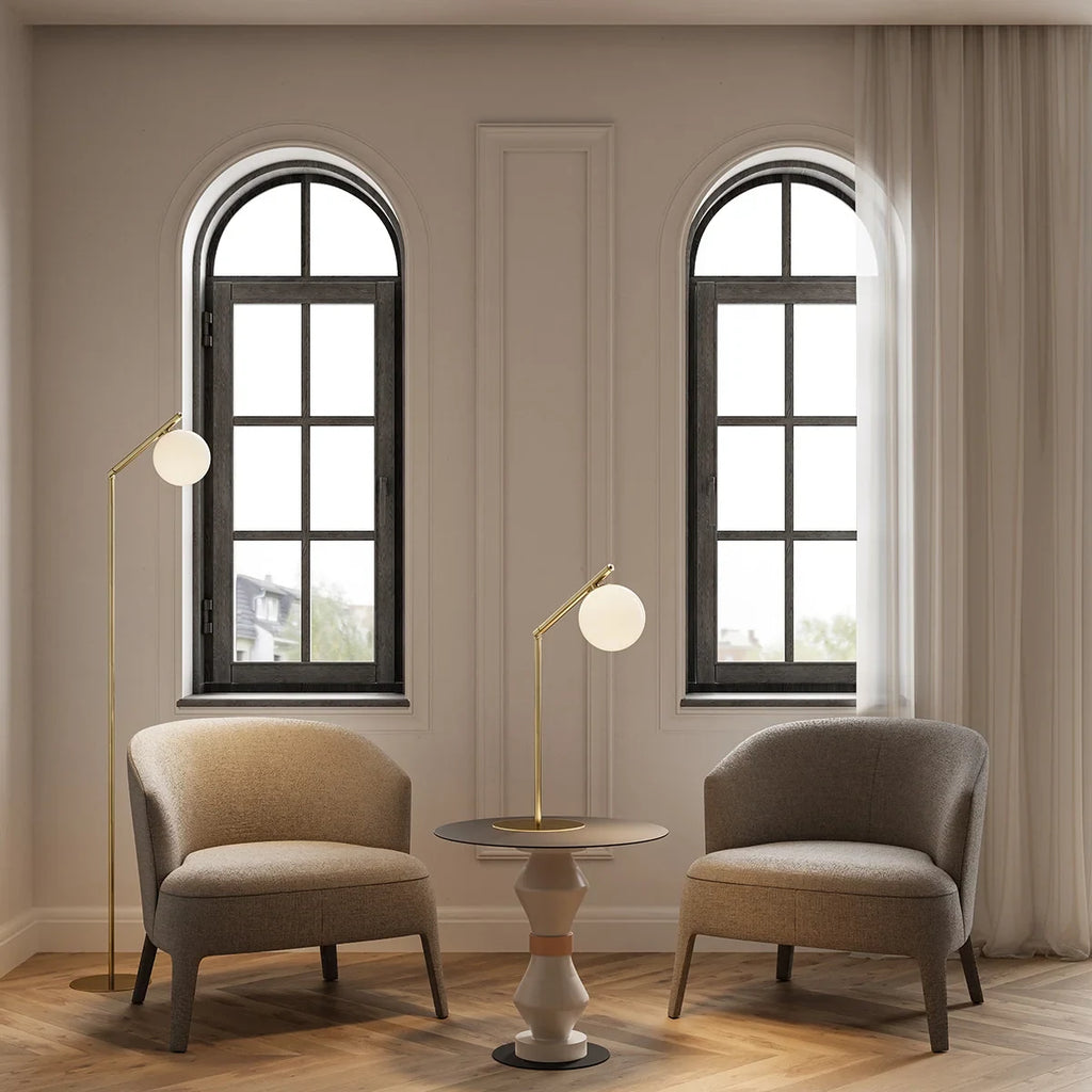 Slim articulated floor lamp with opal glass globe, matte brass, beside an armchair in a room