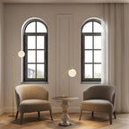 Slim articulated floor lamp with opal glass globe, matte brass, beside an armchair in a room