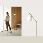 Slim articulated floor lamp with opal glass globe, matte brass, in a bedroom scene