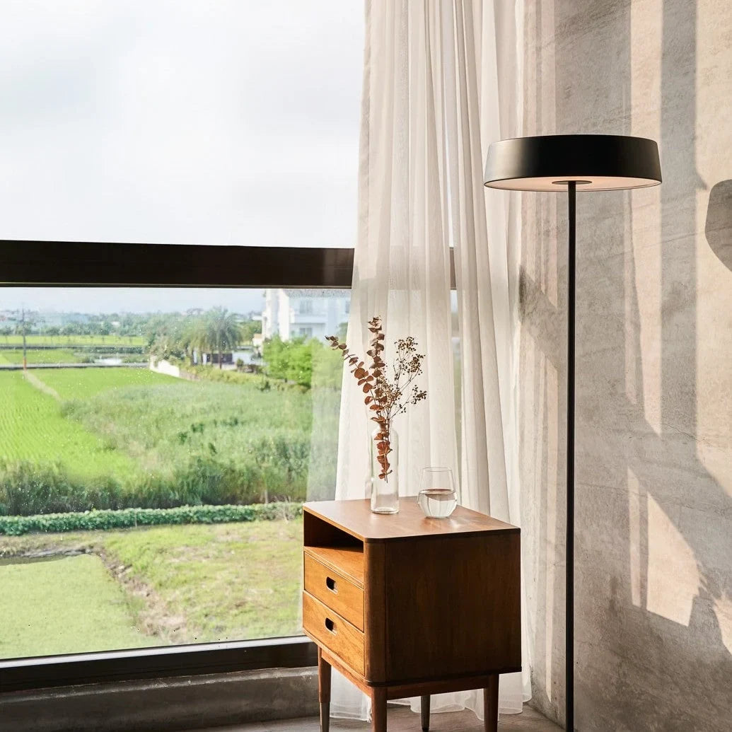 Slim disc LED floor lamp, in black by a window