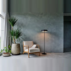 Slim disc LED floor lamp, in black beside an armchair