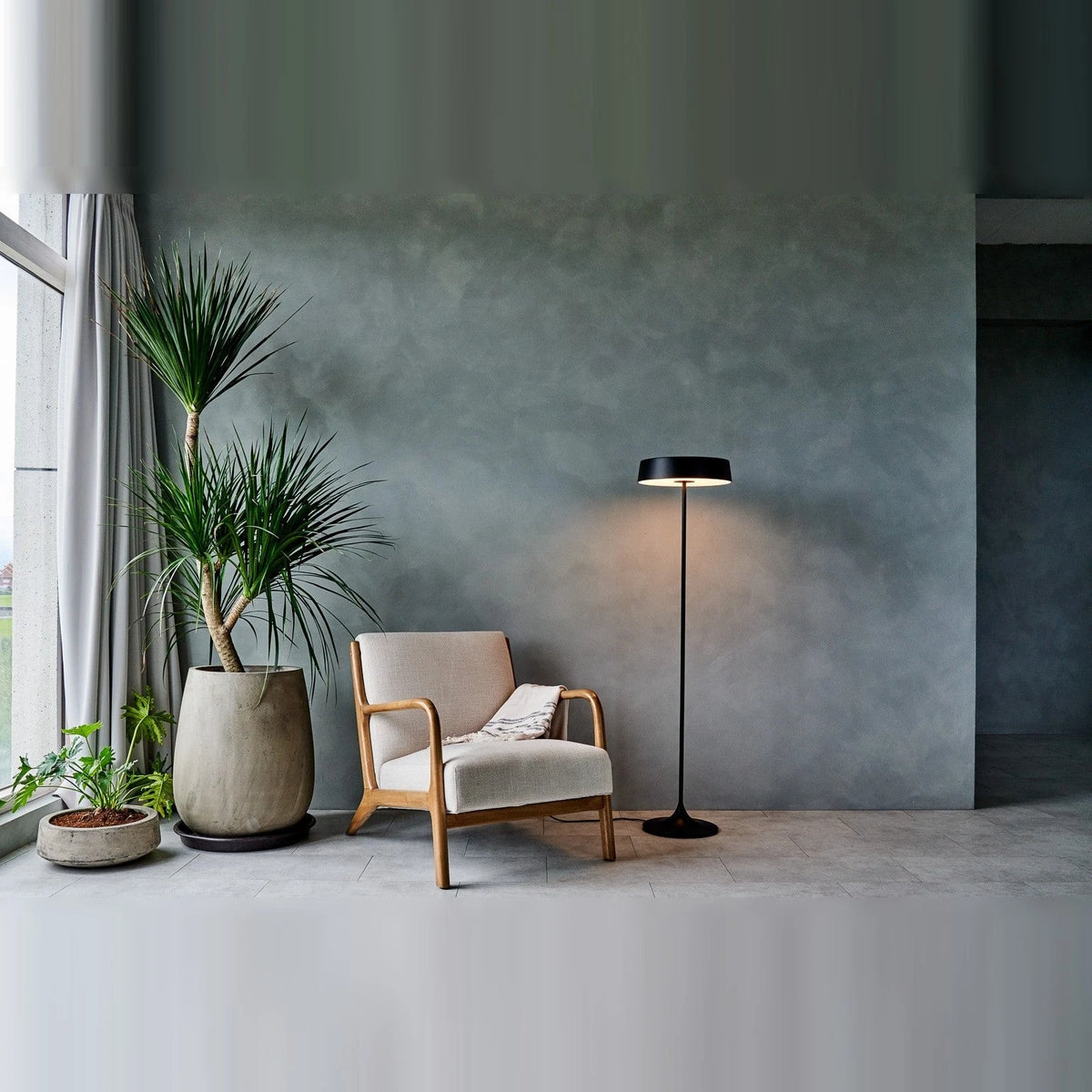 Slim disc LED floor lamp, in black beside an armchair