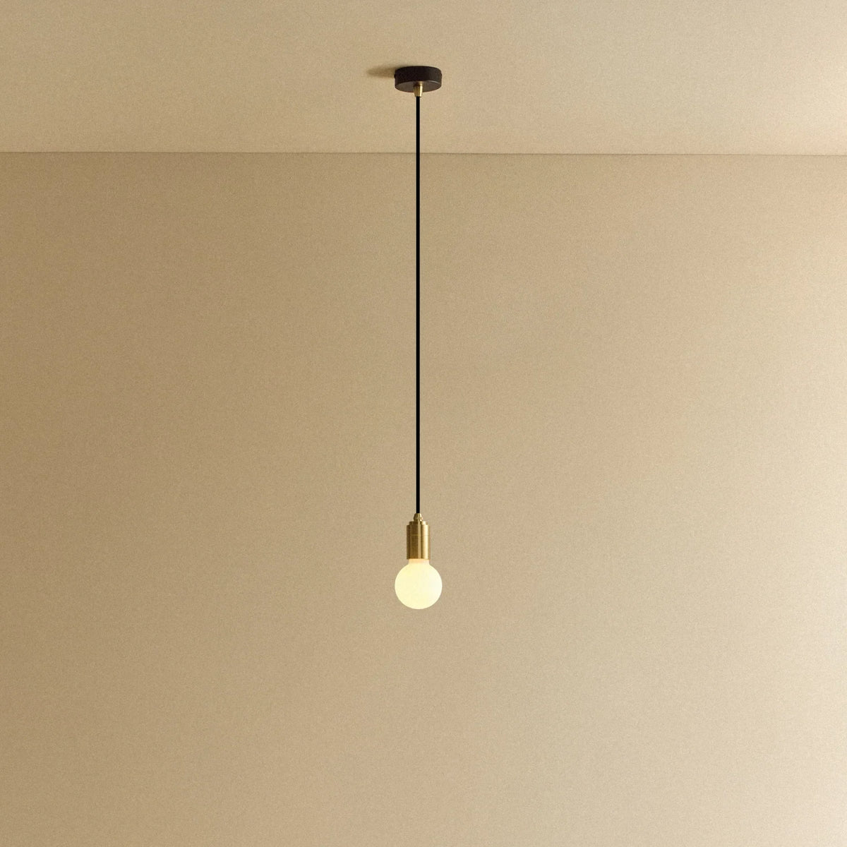 Small opal sphere pendant, in brass, lit, against a plain wall