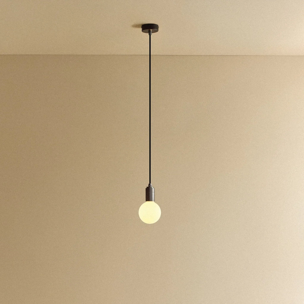 Small squat matte white glass pendant, graphite, lit, against a plain wall