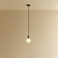 Small squat matte white glass pendant, graphite, lit, against a plain wall