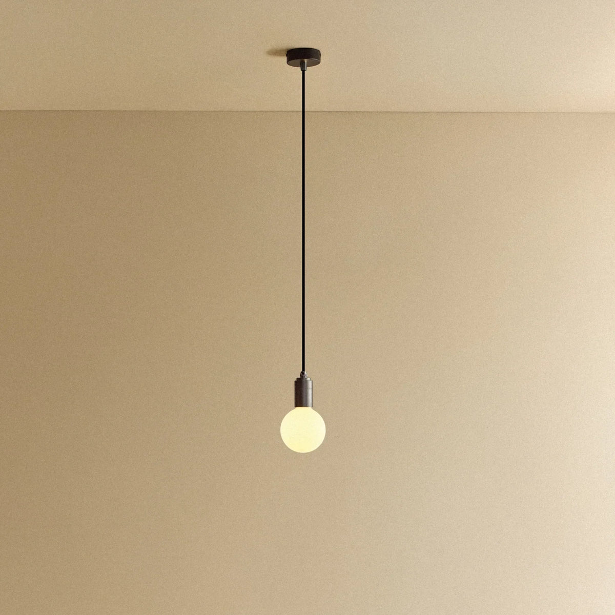 Small squat matte white glass pendant, graphite, lit, against a plain wall