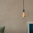 Plug-in pendant with small tinted bulb, graphite, close-up of the lit bulb against a plain wall