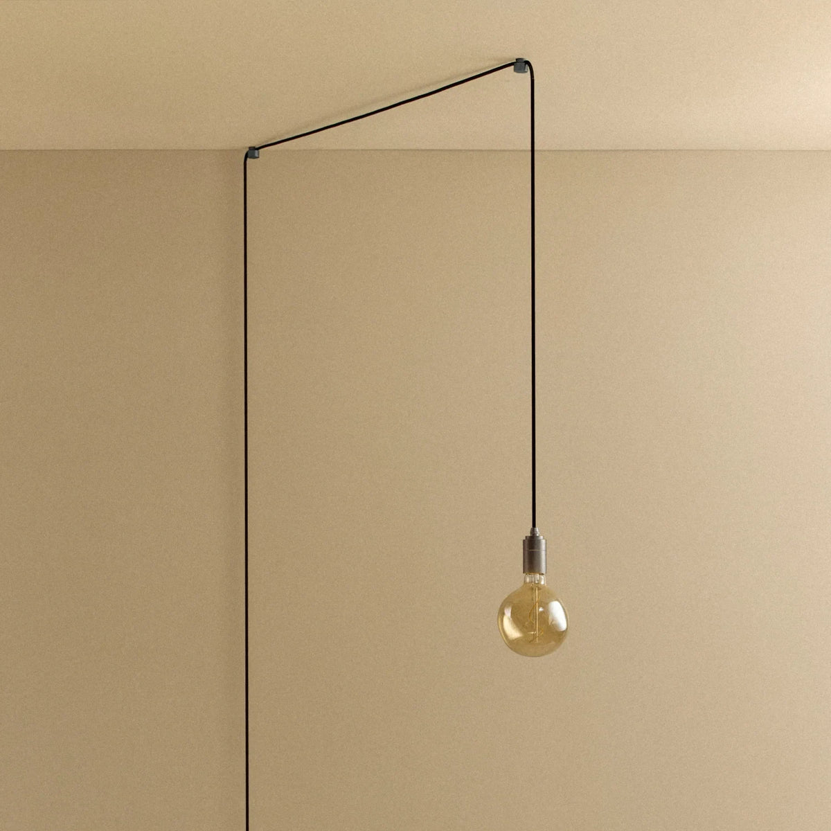Plug-in pendant with small tinted bulb, graphite, lit, hung from a wall node, another angle