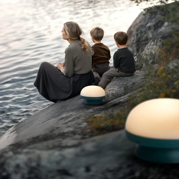Cordless solar dome table lamp in forest green, a family seated by a lamp on a rock