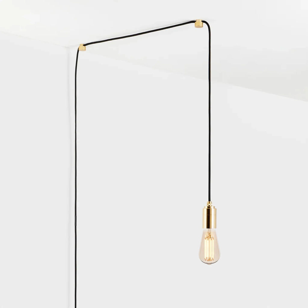 Squirrel cage filament plug-in pendant, in brass, routed across the ceiling and down the wall