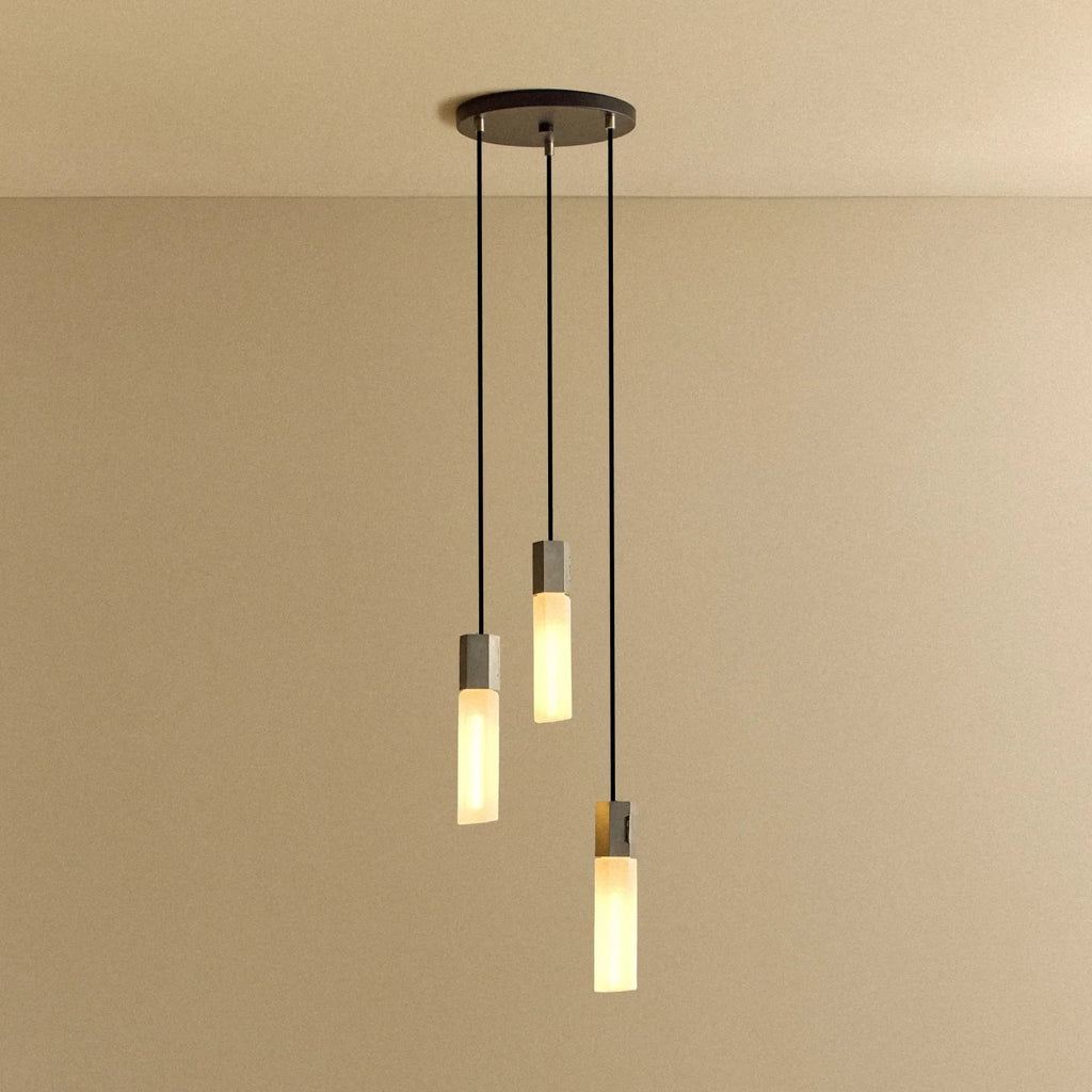 Three-drop cluster pendant in cast stainless steel with glass bulbs, lit, against a plain wall