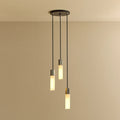 Three-drop cluster pendant in cast stainless steel with glass bulbs, lit, against a plain wall