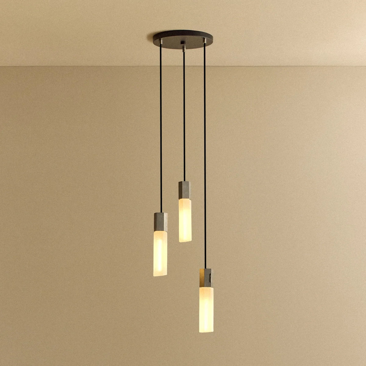 Three-drop cluster pendant in cast stainless steel with glass bulbs, lit, against a plain wall