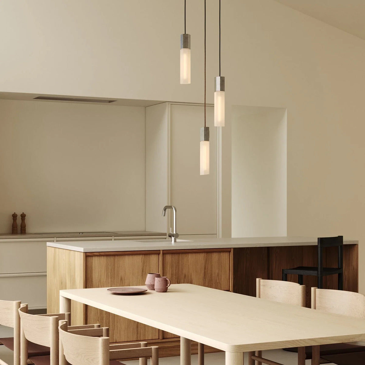 Three-drop cluster pendant in cast stainless steel with glass bulbs, over a kitchen island and dining table