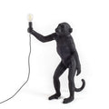 Standing ape figure table lamp in black, holding a bare bulb aloft, on a plain background