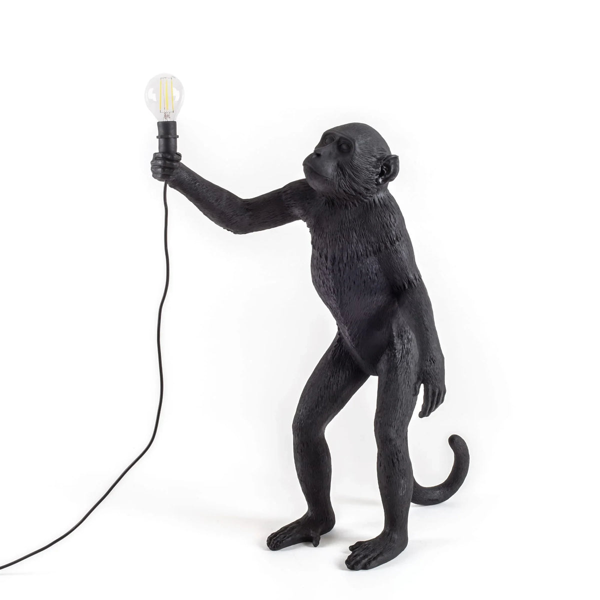Standing ape figure table lamp in black, holding a bare bulb aloft, on a plain background