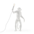 Standing ape figure table lamp in white resin, holding a bare bulb aloft, on a plain background