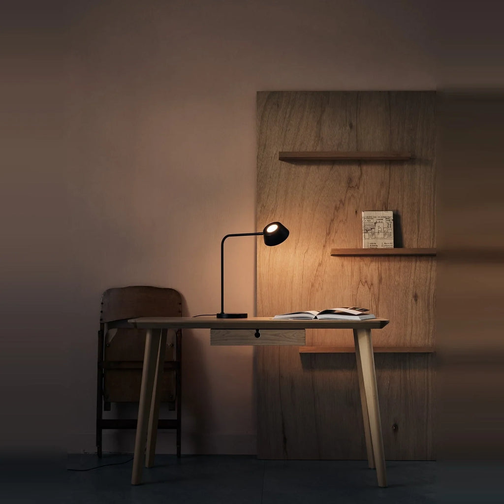 Slim desk table lamp with rotating shade, lit on a desk in a dim room