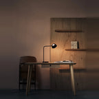 Slim desk table lamp with rotating shade, lit on a desk in a dim room