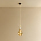 Tall tinted bulb pendant, in brass, lit, against a plain wall
