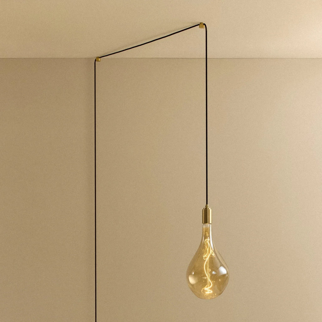 Tall tinted bulb plug-in pendant, in brass, routed across the ceiling and down the wall