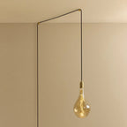 Tall tinted bulb plug-in pendant, in brass, routed across the ceiling and down the wall