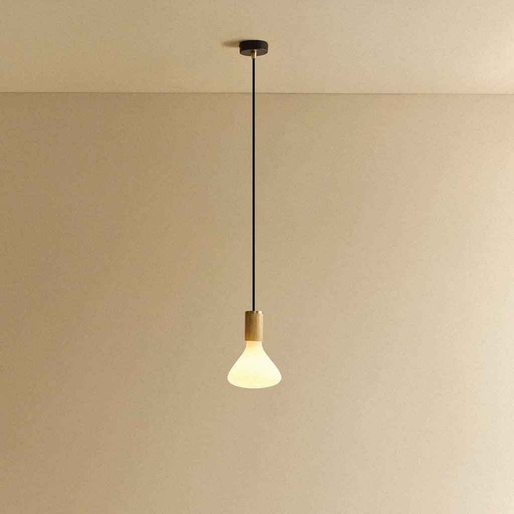 Tapered matte white bulb pendant, oak, lit, against a plain wall