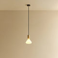 Tapered matte white bulb pendant, oak, lit, against a plain wall