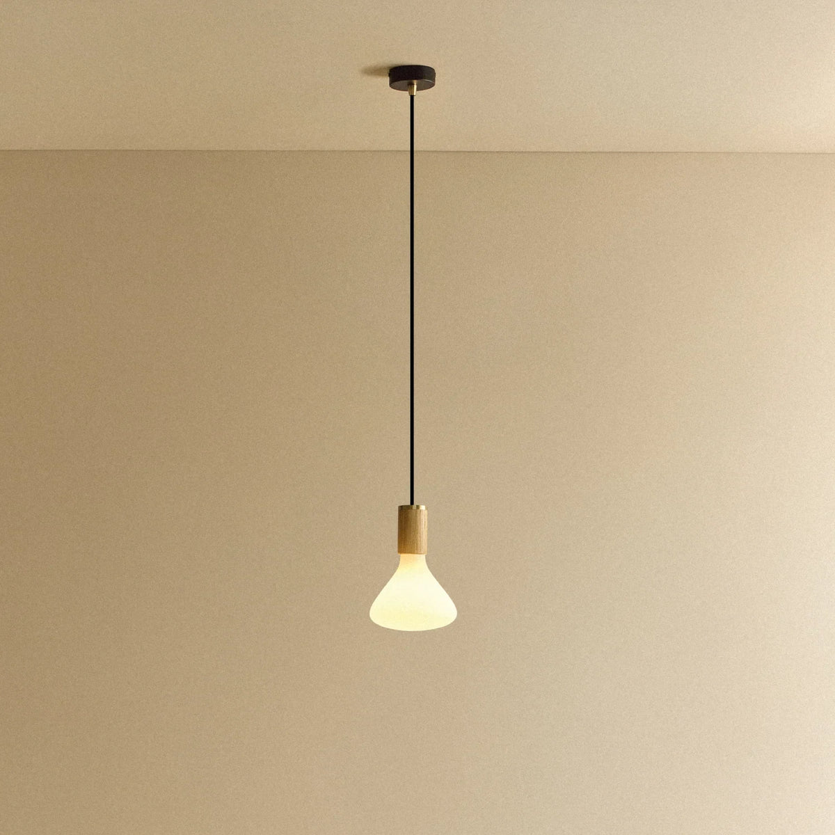 Tapered matte white bulb pendant, oak, lit, against a plain wall