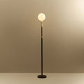 Brass telescopic floor lamp with a globe bulb, lit, on a plain background