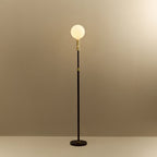 Brass telescopic floor lamp with a globe bulb, lit, on a plain background