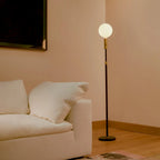 Brass telescopic floor lamp with a globe bulb, beside a sofa in a living room