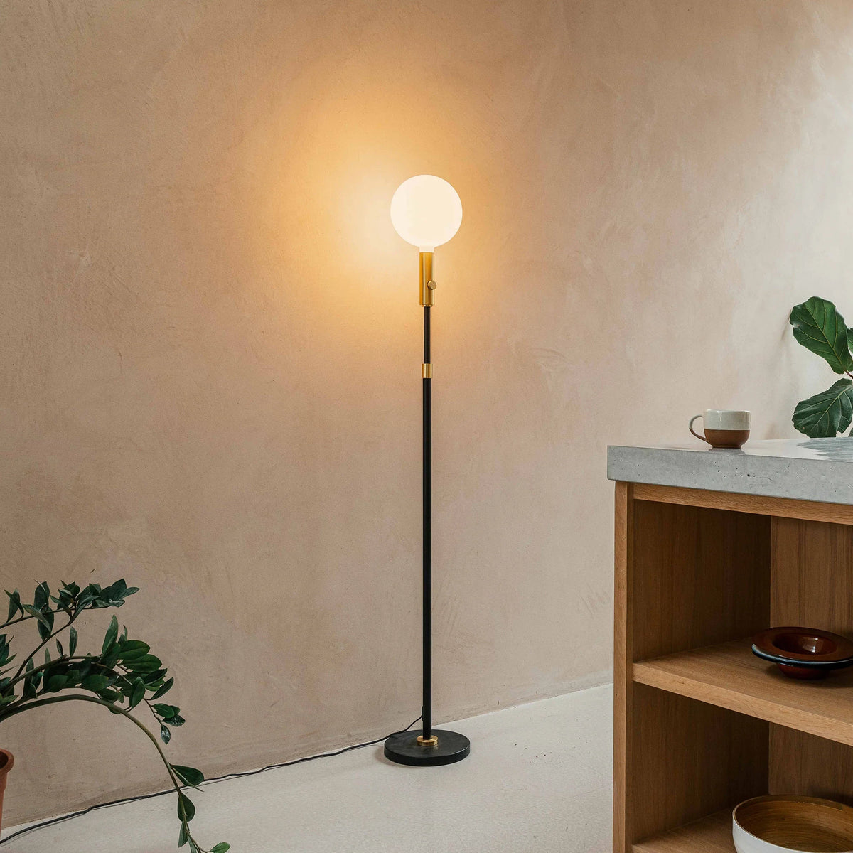 Brass telescopic floor lamp with a globe bulb, lit beside a shelf in a room corner