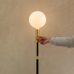 Brass telescopic floor lamp with a globe bulb, hand on the brass stem below the globe bulb