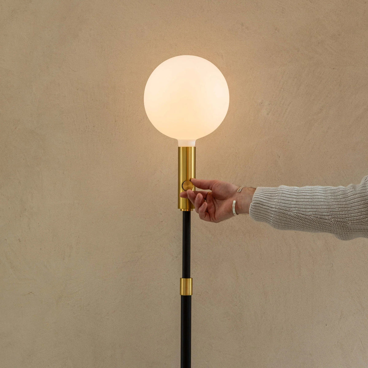 Brass telescopic floor lamp with a globe bulb, hand on the brass stem below the globe bulb