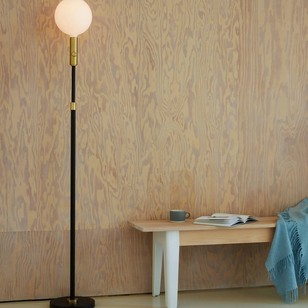 Brass telescopic floor lamp with a globe bulb, beside a bench against a plaster wall