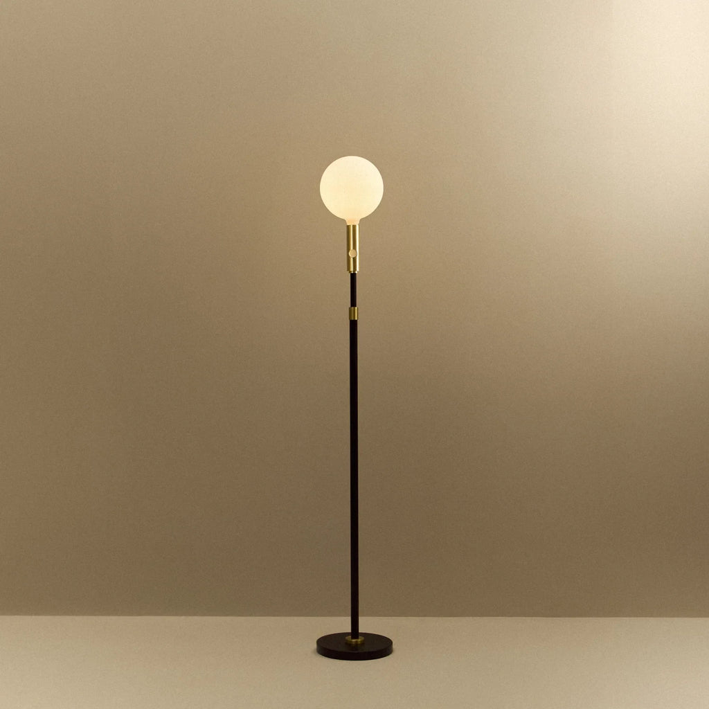 Brass telescopic floor lamp with a globe bulb, lit, on a plain background