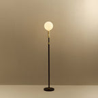 Brass telescopic floor lamp with a globe bulb, lit, on a plain background