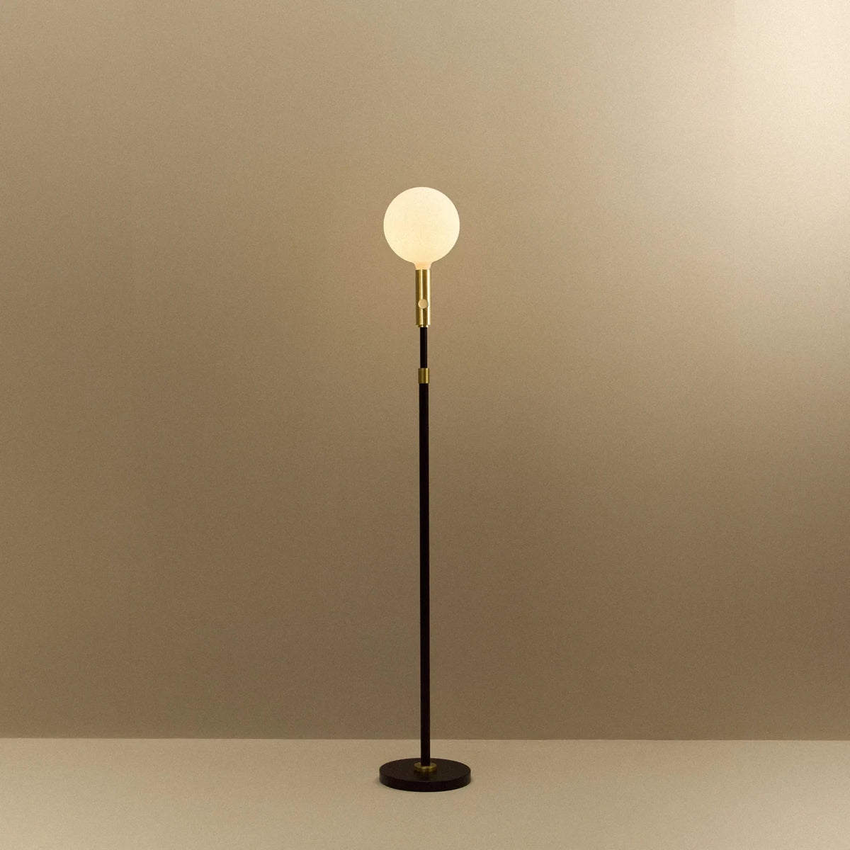 Brass telescopic floor lamp with a globe bulb, lit, on a plain background