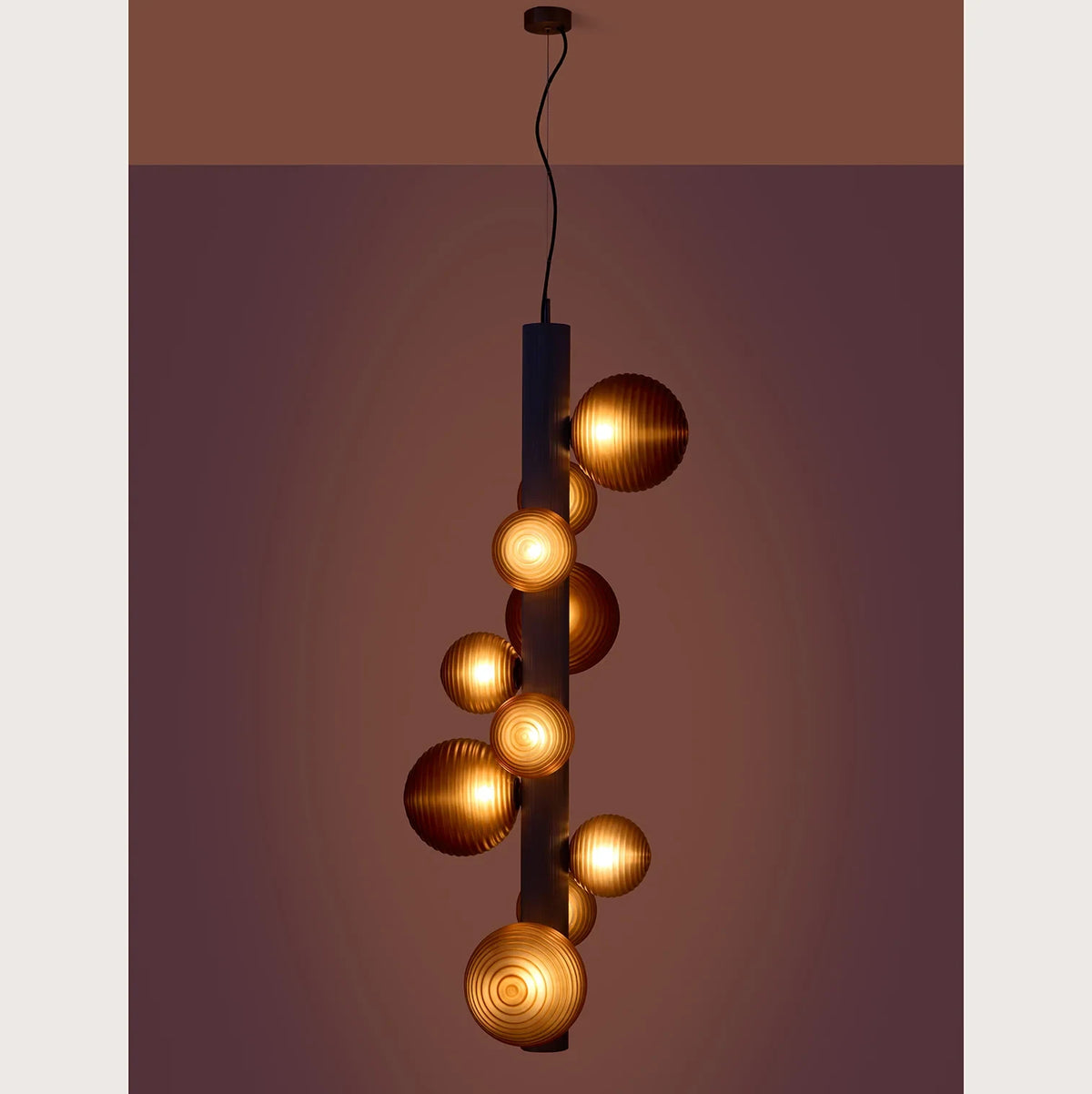 Ten-globe glass tube pendant, lit against a dark wall
