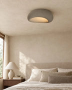 Textured pebble flush ceiling light, in grey, above a bed