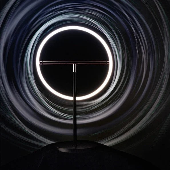 Tilting ring LED table lamp, black and copper, lit ring in a dark setting