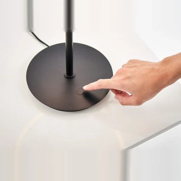 Tilting ring LED table lamp, black and copper, a finger touching the dimmer on the base