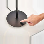 Tilting ring LED table lamp, black and copper, a finger touching the dimmer on the base