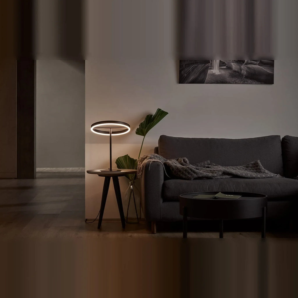 Tilting ring LED table lamp, black and copper, beside a sofa in a living room